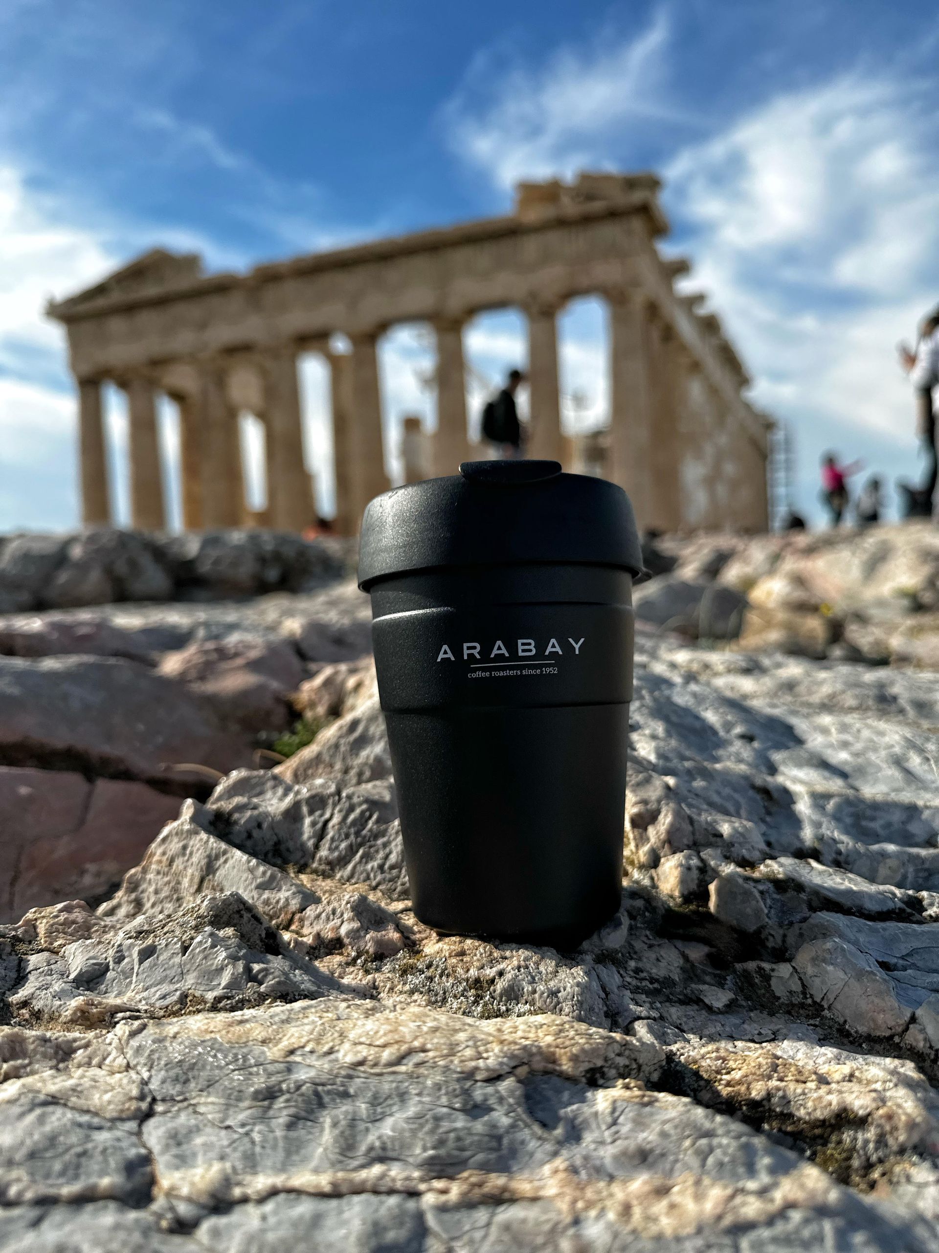 Una taza de café negro sobre una roca frente a un edificio.