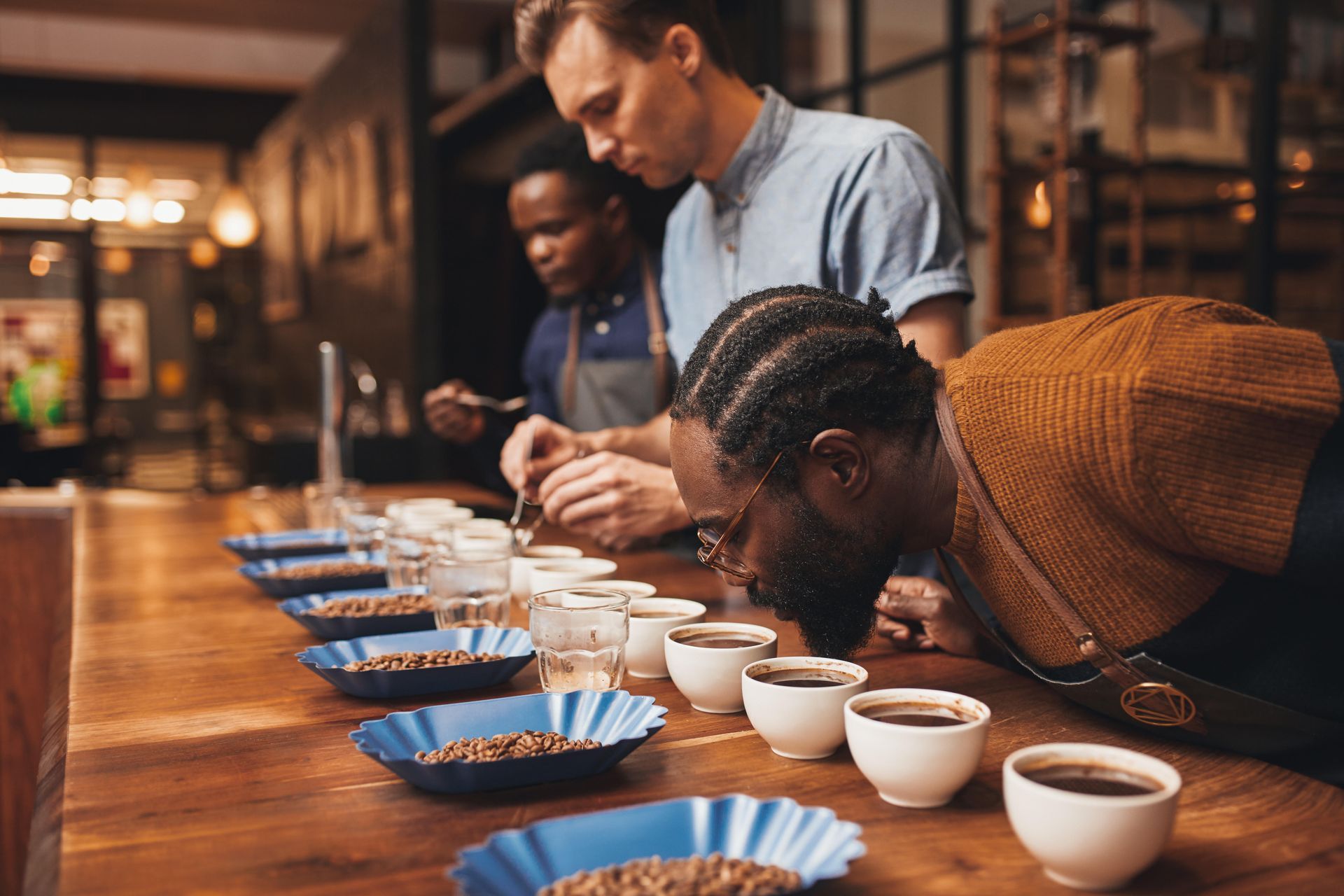 Un grupo de personas sentadas en una mesa oliendo granos de café.